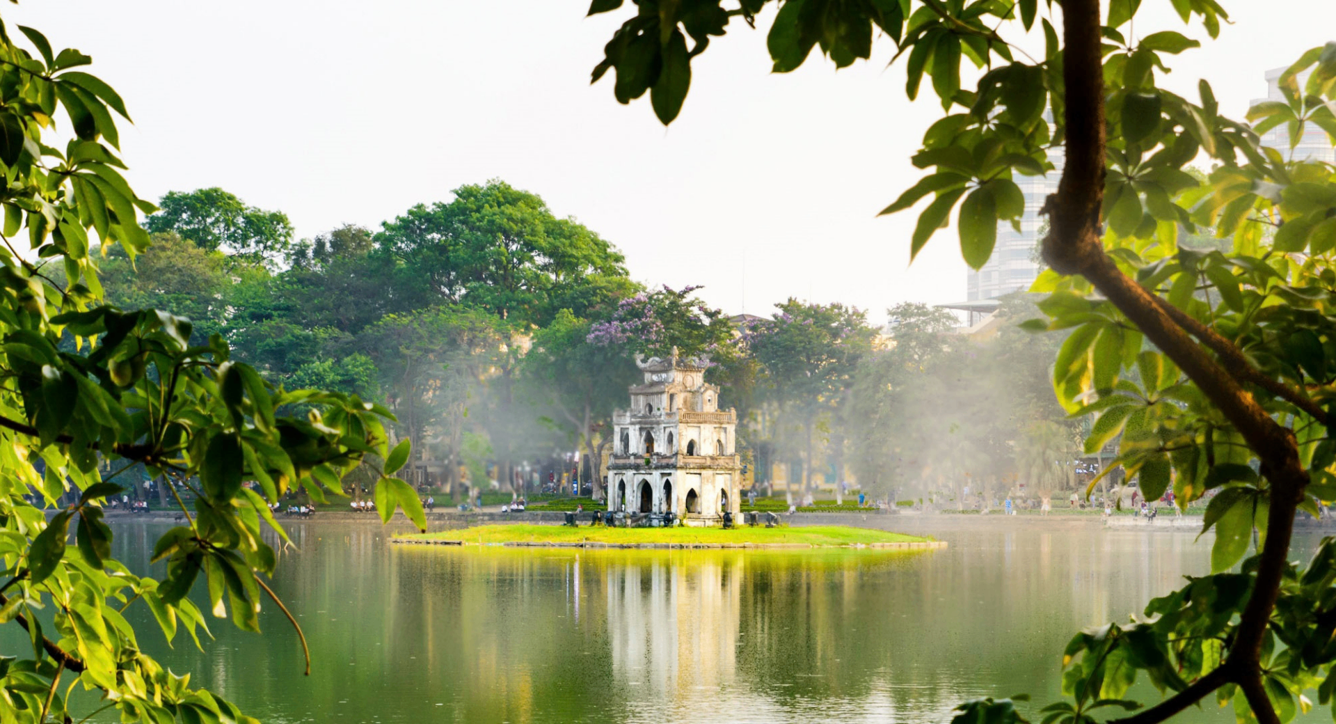 Hoan Kiem Lake in Ha Noi framed by trees in soft morning light.