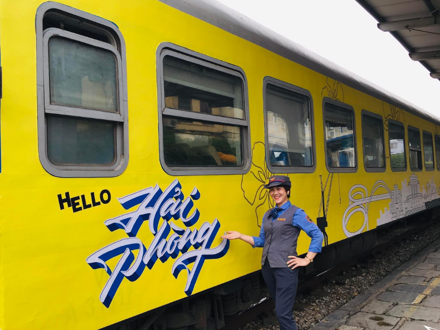 Bright yellow Hai Phong train with staff member beside it.