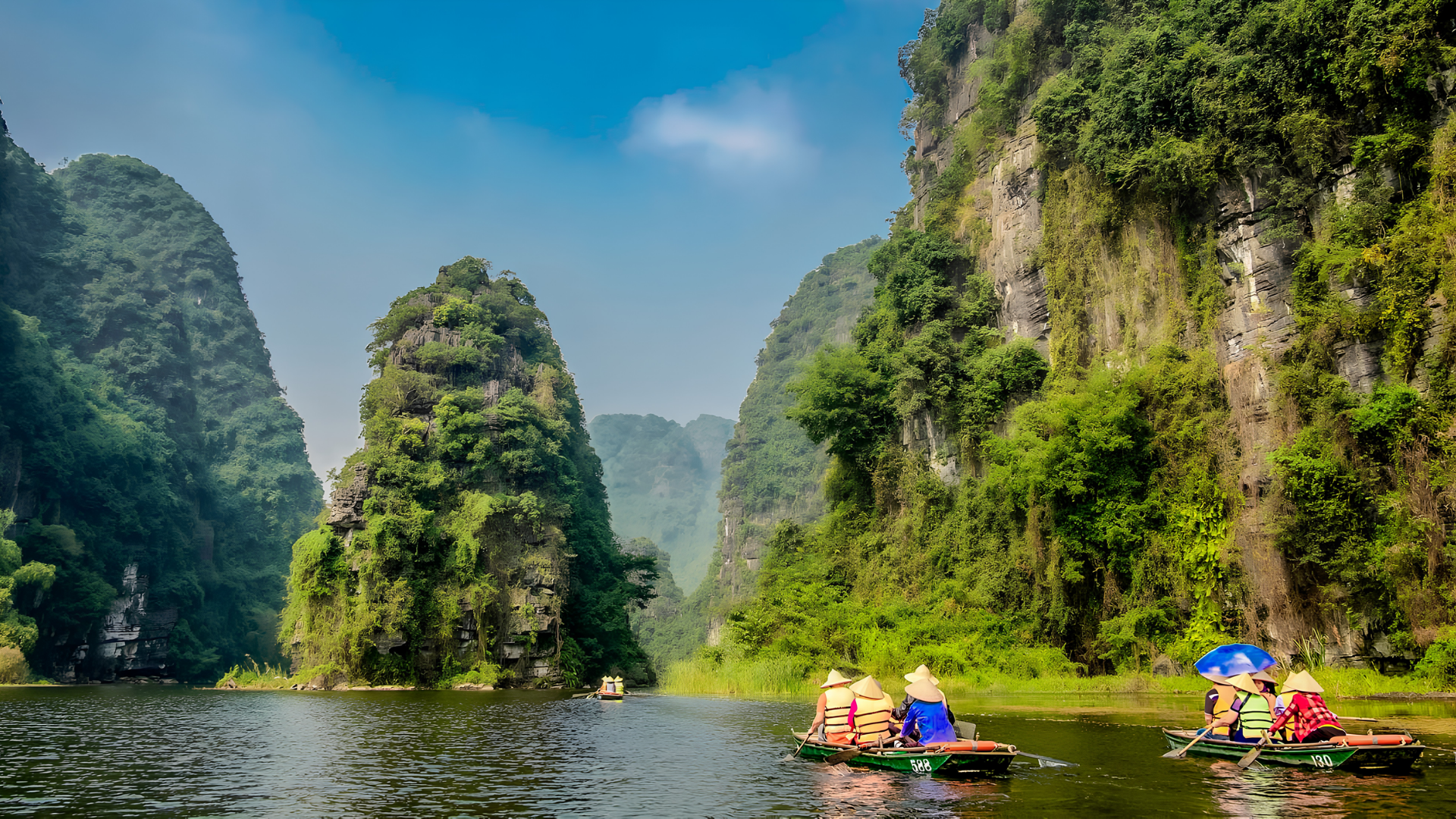 Visitors in boats moving through Trang An river landscape.